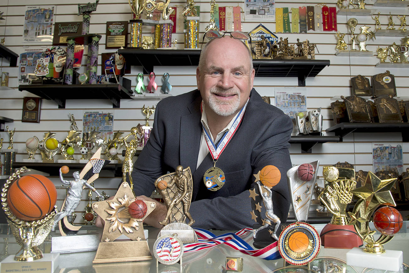 Keith Baldwin, 58, president of Spike’s Trophies in Philadelphia, displays participation trophies on the counter. Baldwin himself participated in a triathlon recently and made a participation medal (like the one hanging around his neck) for himself. (Clem Murray/Philadelphia Inquirer)