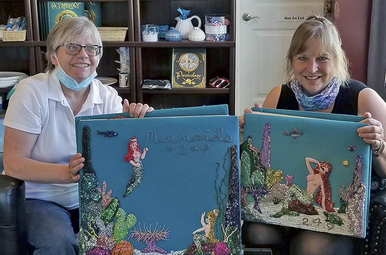 Courtesy photo                                Hoquiam librarian Mary Thornton, left, and International Mermaid Museum director Kim Roberts display scrapbooks featuring handmade art from an organization called the Mermaids, which was active on Grays Harbor between World War I and the late 1970s.