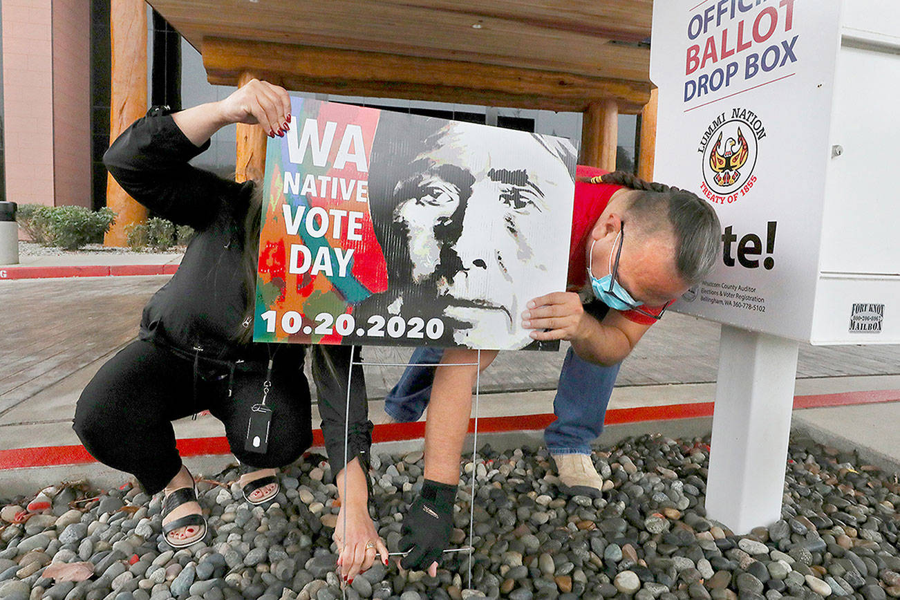 Lummi tribal members Teresa Taylor and Freddie Lane secure a Washington Native Vote Day sign outside the tribe's Administration Building on Oct. 7, north of Bellingham. The image on the sign is one by Edward Curtis titled "Lummi Woman" from 1899, modified to encourage Lummi tribal members to vote. (Alan Berner/Seattle Times)