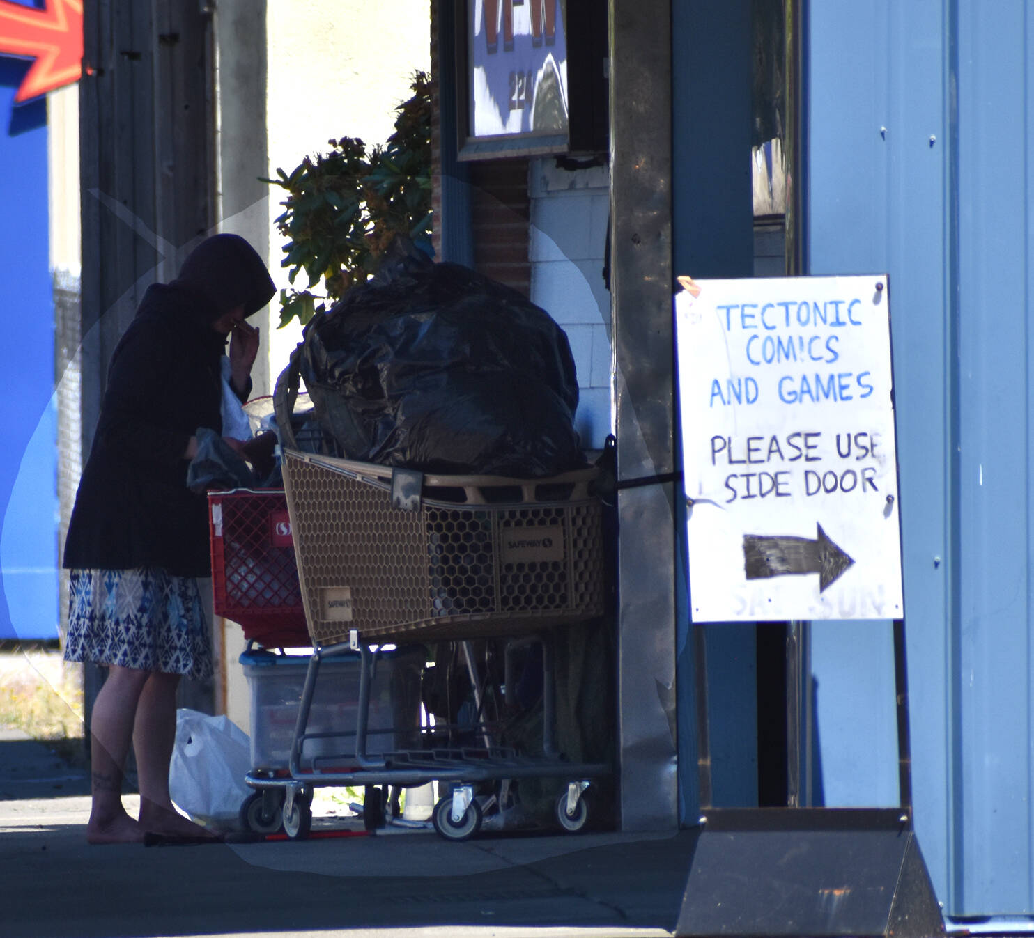 A woman stands near a used Safeway cart out on the south side of Heron Street in downtown Aberdeen. While a Safeway cart is photographed here, there are wayward carts from a variety of stores. The city of Aberdeen has been proposing an ordinance to put the onus on the stores to wrangle their carts. (Matthew N. Wells / The Daily World)