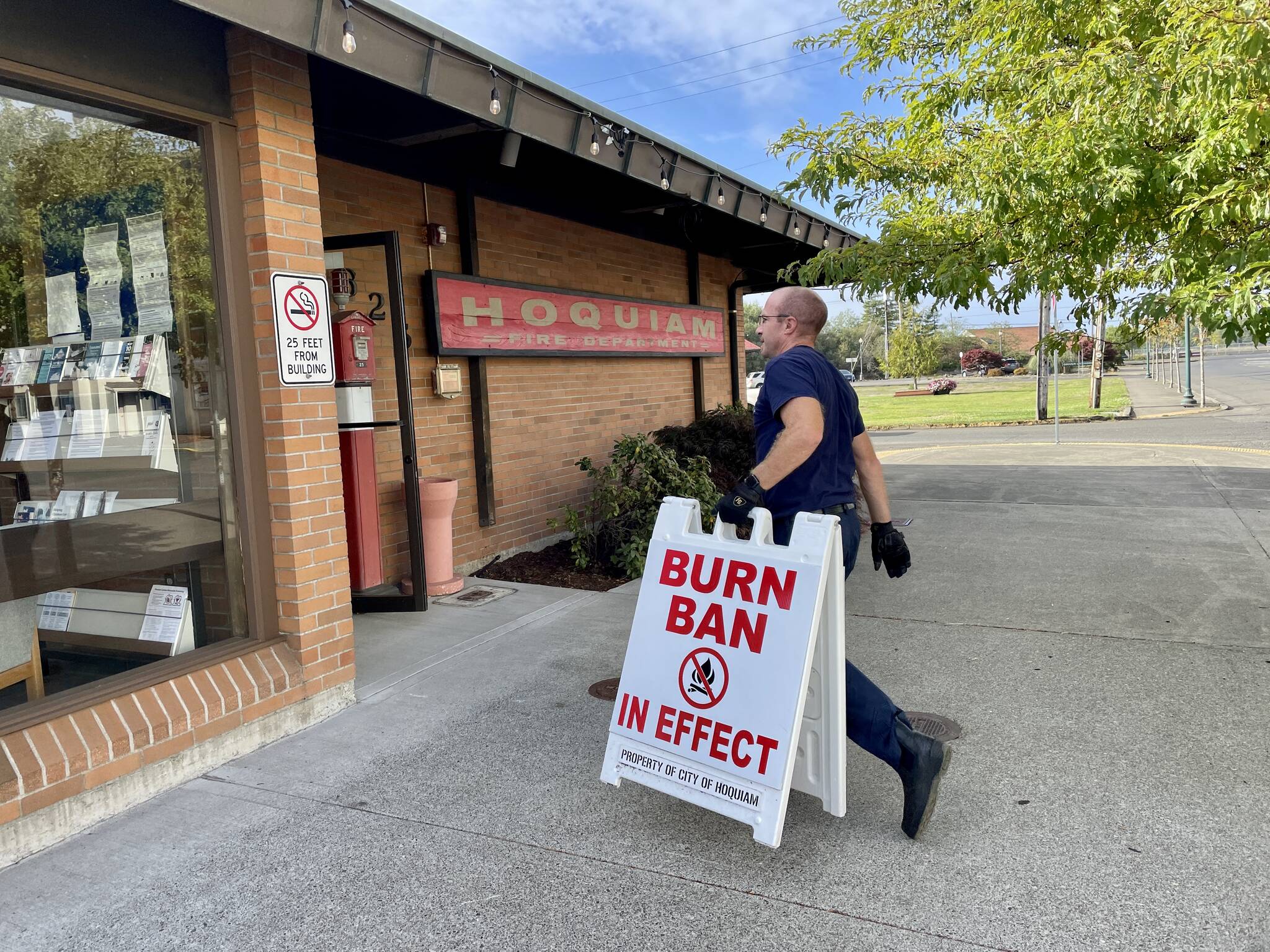 Hoquiam fire Capt. Brandon Ray carries in a burn ban sign as the county eases restrictions with the advent of cooler, damper fall weather on September 19. (Michael S. Lockett / The Daily World)