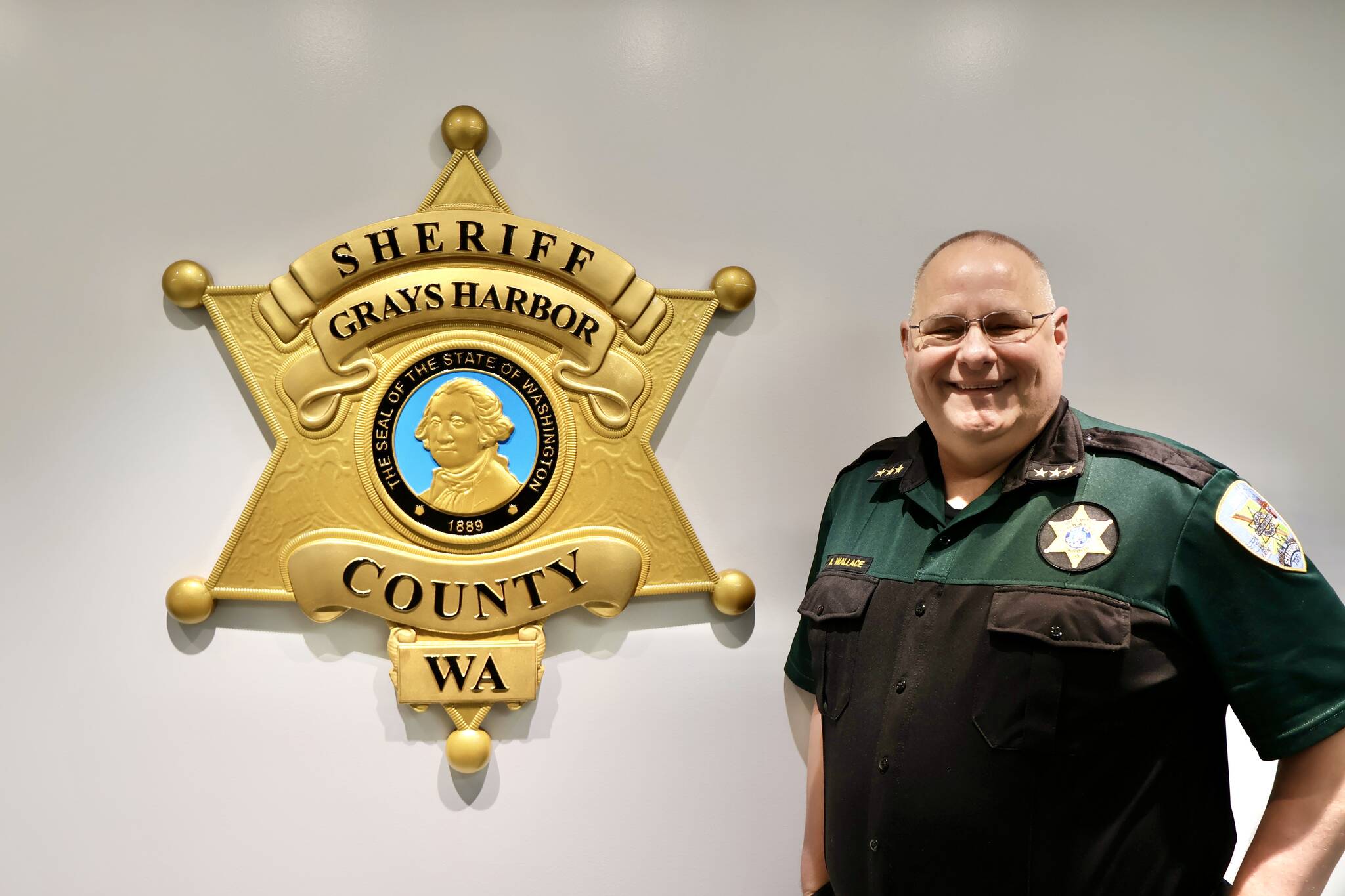 Sheriff Darrin Wallace stands alongside the agency’s new crest in their Montesano headquarters. (Michael S. Lockett / The Daily World)