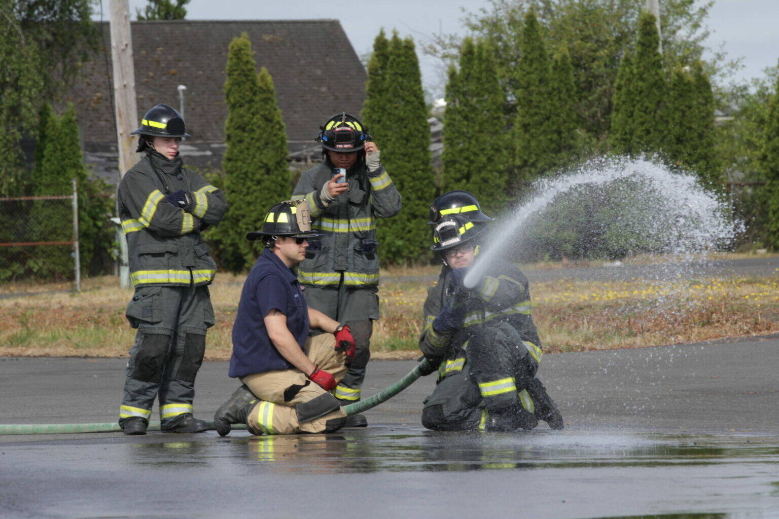 Derek Jensen of the Hoquiam Fire Department, in blue T-shirt, teaches a group of high schoolers taking part in a fire science program about using a firehose in 2023. (Michael S. Lockett / The Daily World)